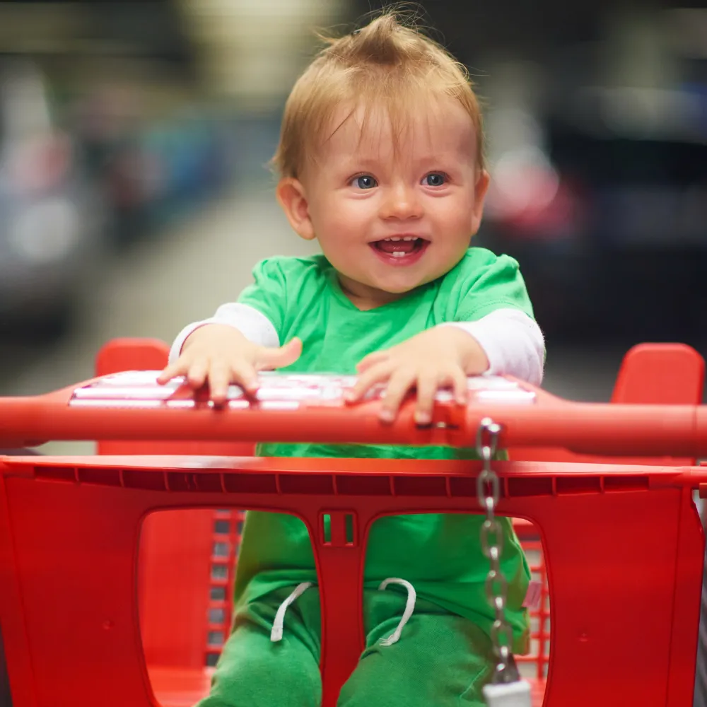 Close-up of an attentive baby seated in a shopping cart, safety straps in place.